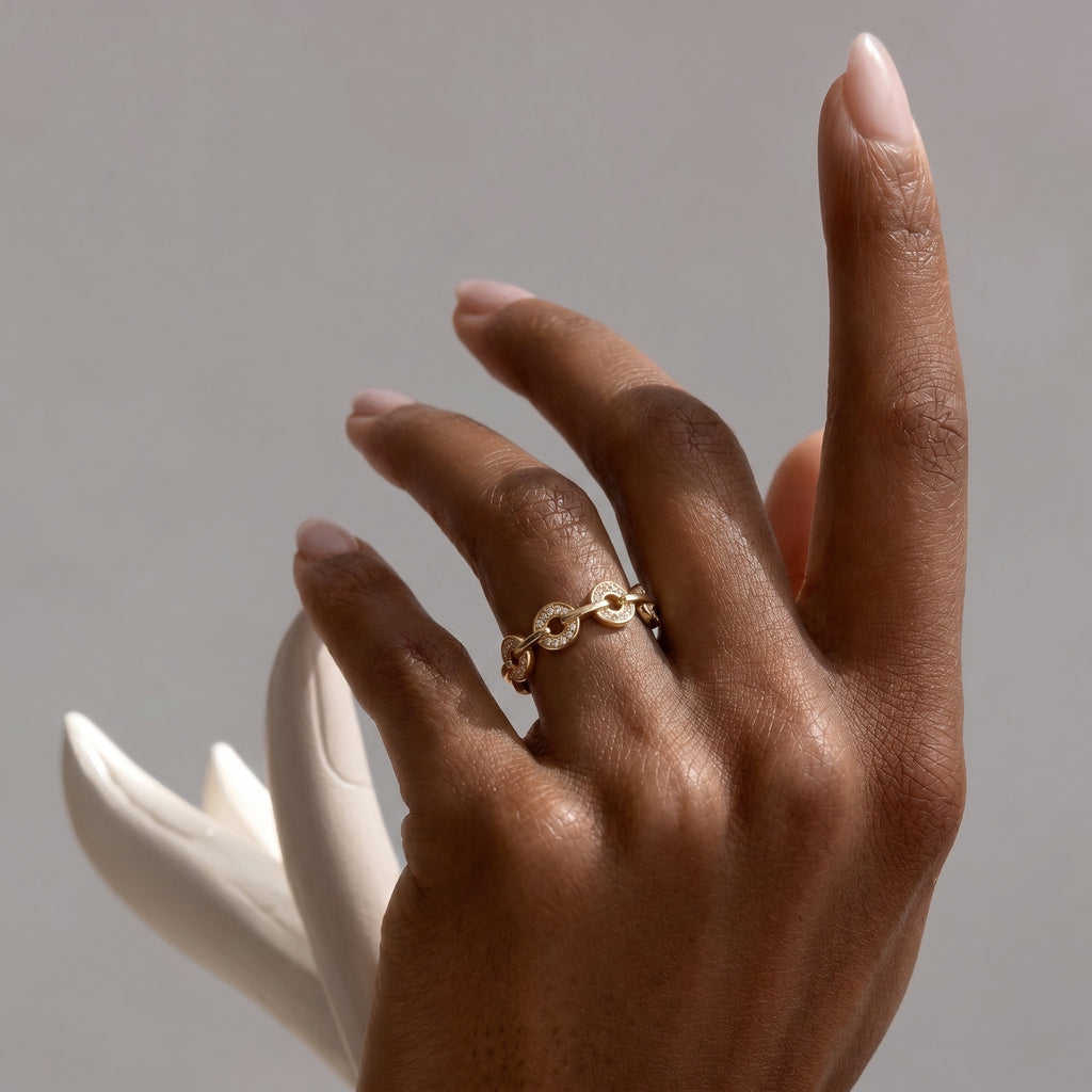 A close-up shot of an elegant hand showcasing the gold-plated Pavé Link Ring, highlighting its intricate design and sparkle against a soft, muted background.
