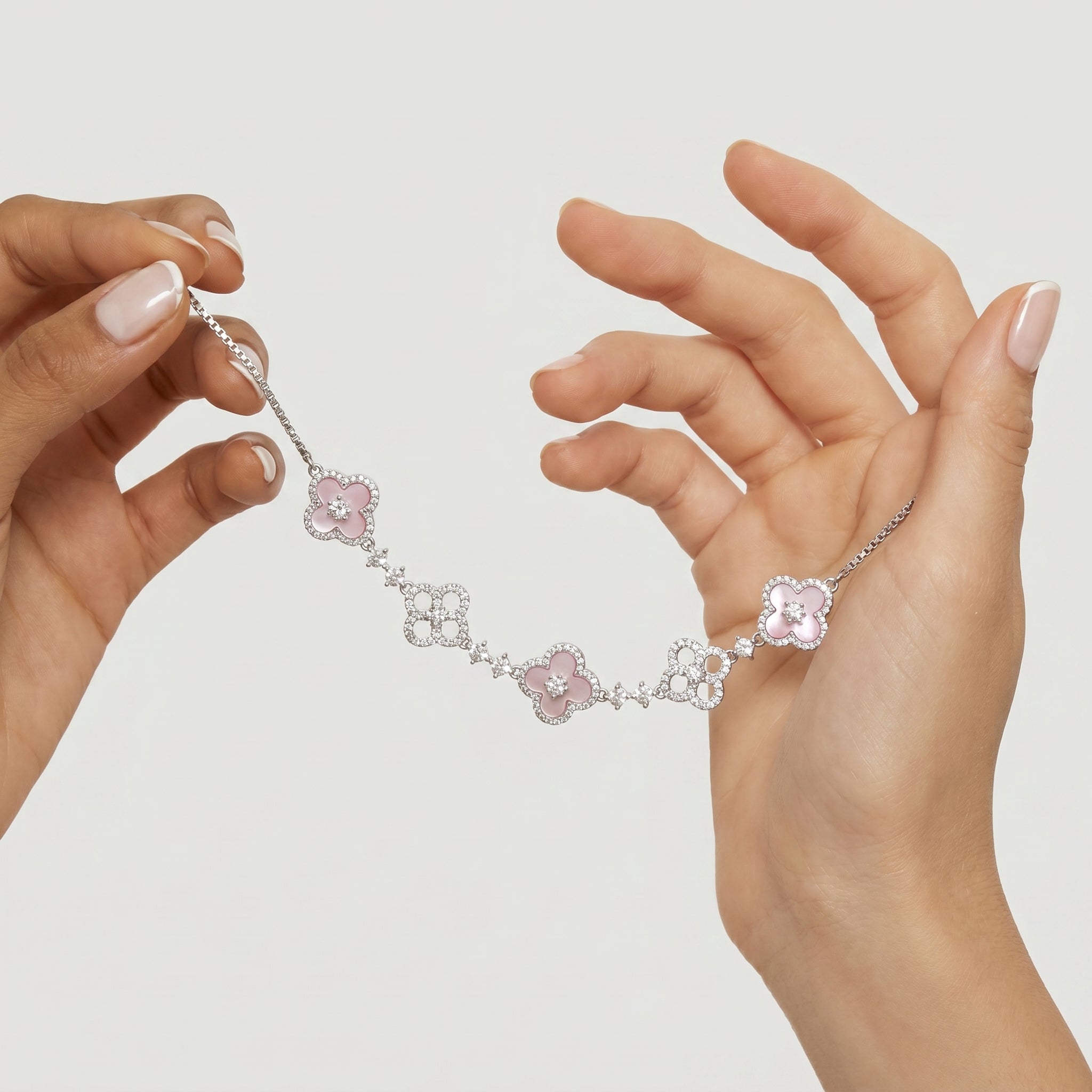 Two hands gently holding the silver-toned Clover Bloom bolo bracelet, showcasing its pink enamel-effect clovers and sparkling simulated diamonds, against a soft, light background.