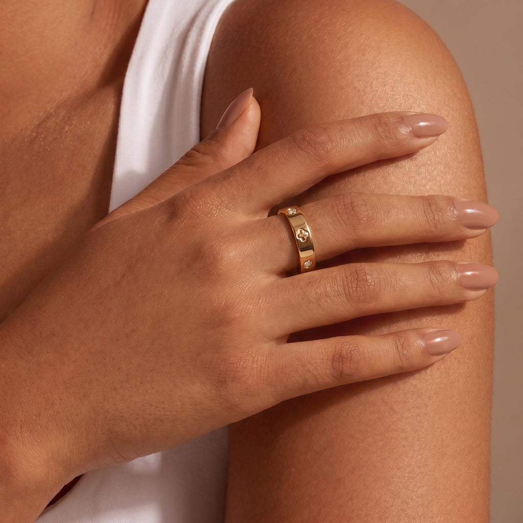 Close-up of a woman's hand with manicured nails, showcasing an 18K gold band featuring a clover motif and diamonds, resting elegantly on her arm.