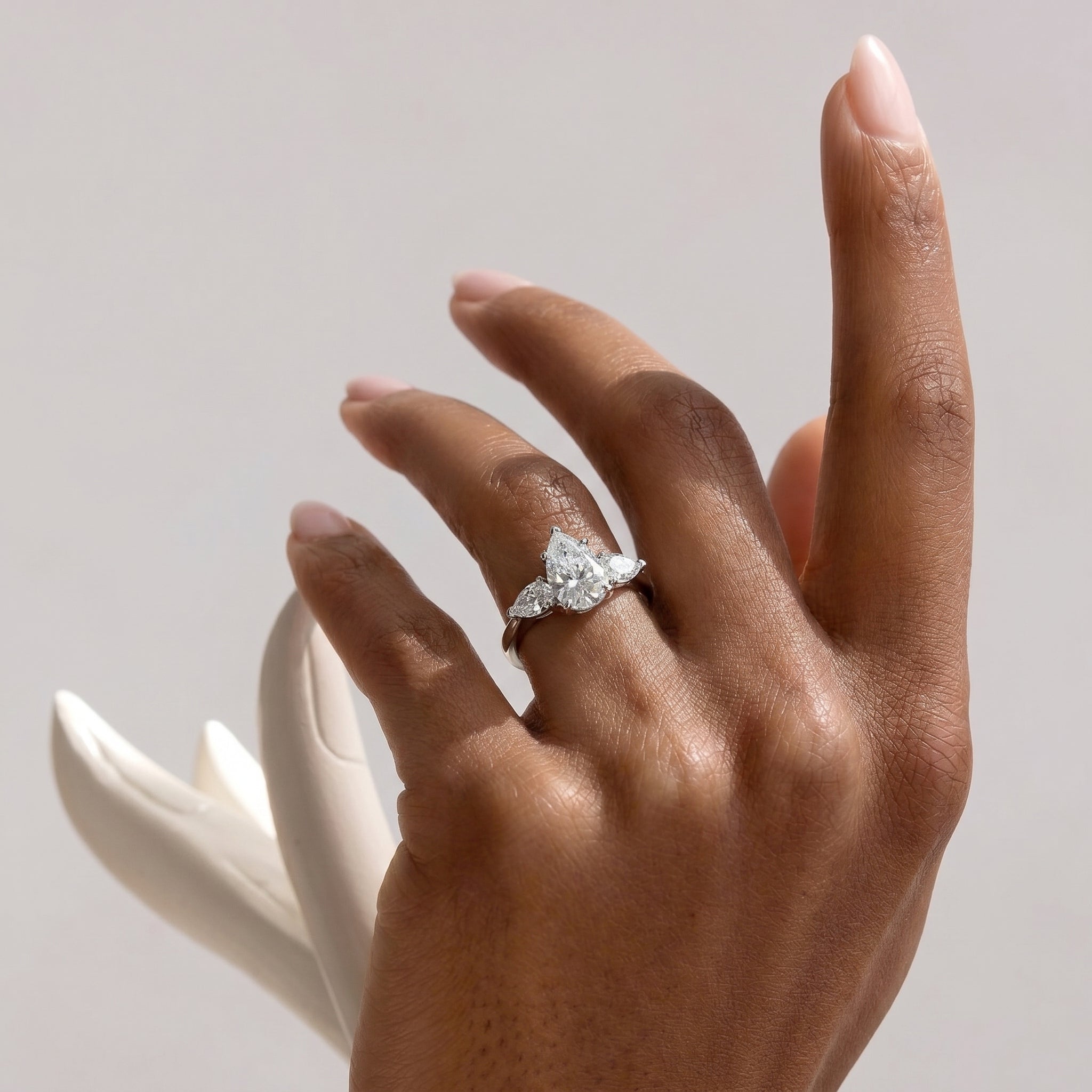 A hand with meticulously manicured nails gracefully displaying the pear cut three-stone cubic zirconia ring on the ring finger, set against a soft, light background with subtle shadows.