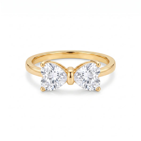 Golden ring with two heart-shaped clear stones forming a delicate bow, centered on a clean white background, showcasing its intricate design and brilliant sparkle.