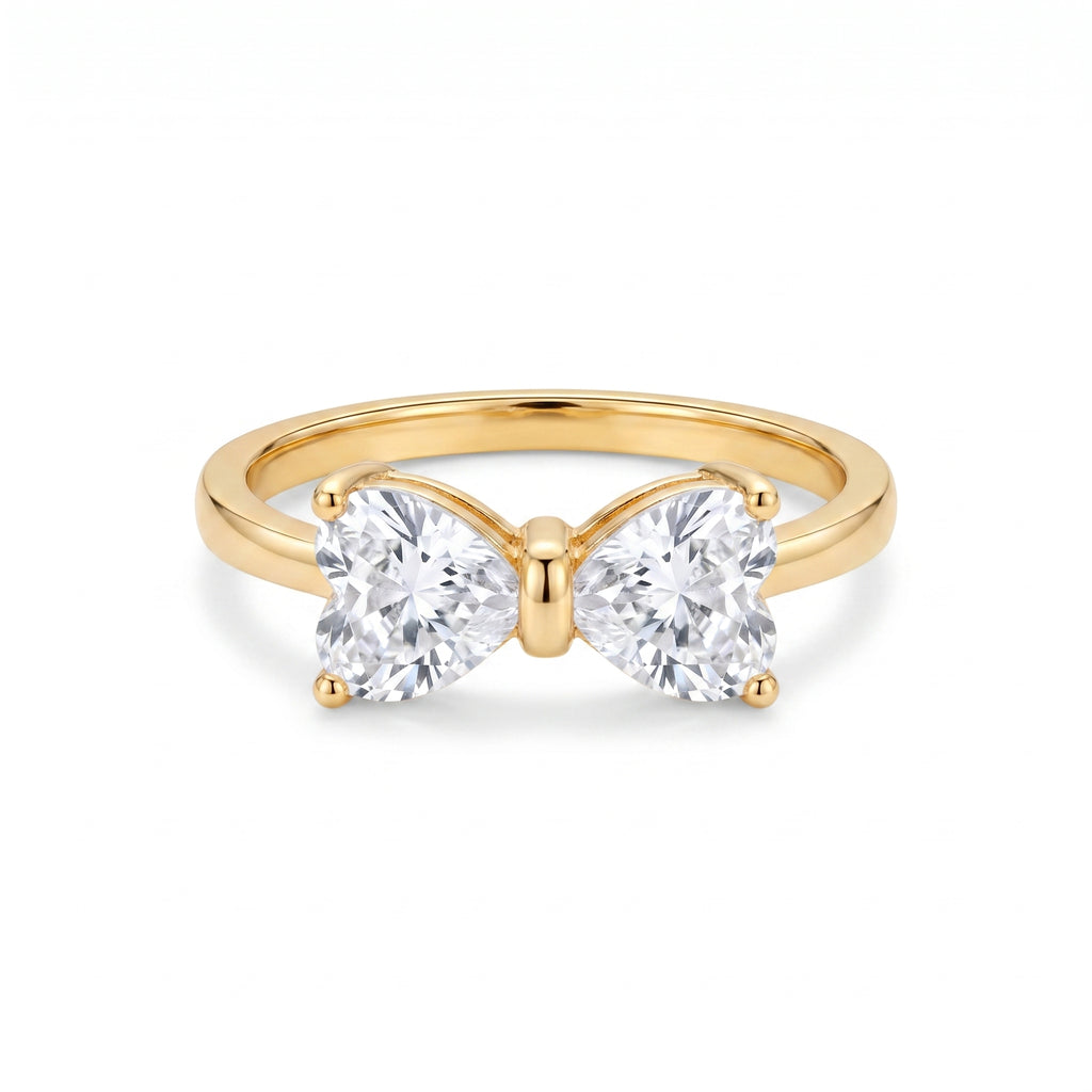 Golden ring with two heart-shaped clear stones forming a delicate bow, centered on a clean white background, showcasing its intricate design and brilliant sparkle.