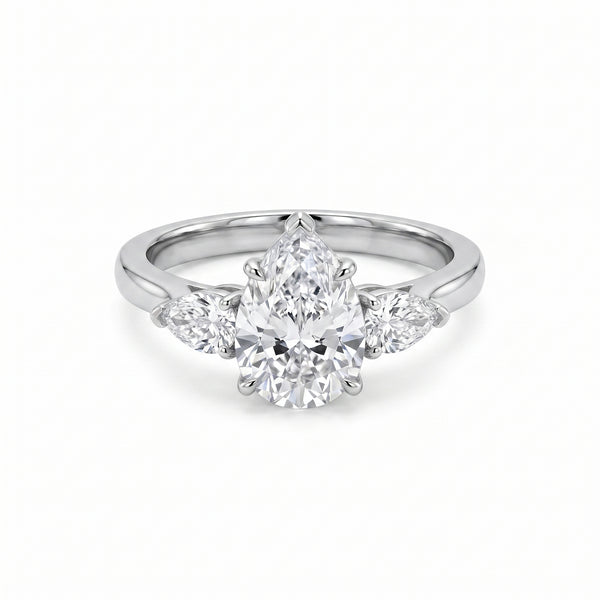 Close-up of a luxurious three-stone ring featuring a pear-cut cubic zirconia center stone flanked by two smaller pear-cut cubic zirconia side stones, set in a gleaming white gold plated band on a pristine white background.