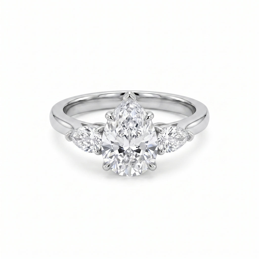 Close-up of a luxurious three-stone ring featuring a pear-cut cubic zirconia center stone flanked by two smaller pear-cut cubic zirconia side stones, set in a gleaming white gold plated band on a pristine white background.
