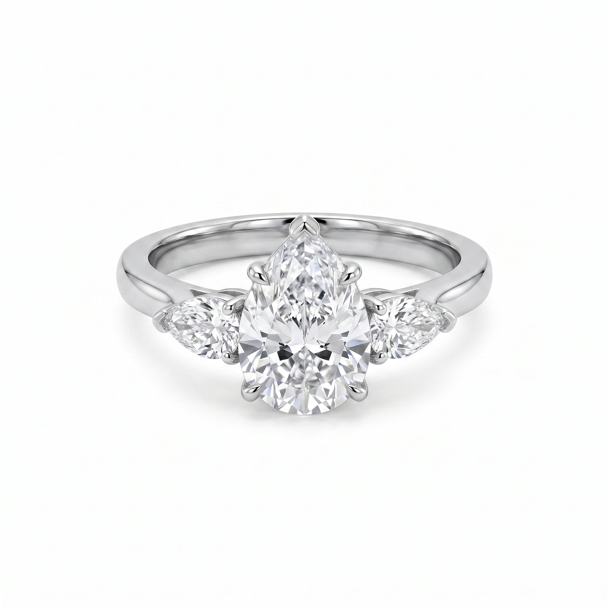 Close-up of a luxurious three-stone ring featuring a pear-cut cubic zirconia center stone flanked by two smaller pear-cut cubic zirconia side stones, set in a gleaming white gold plated band on a pristine white background.