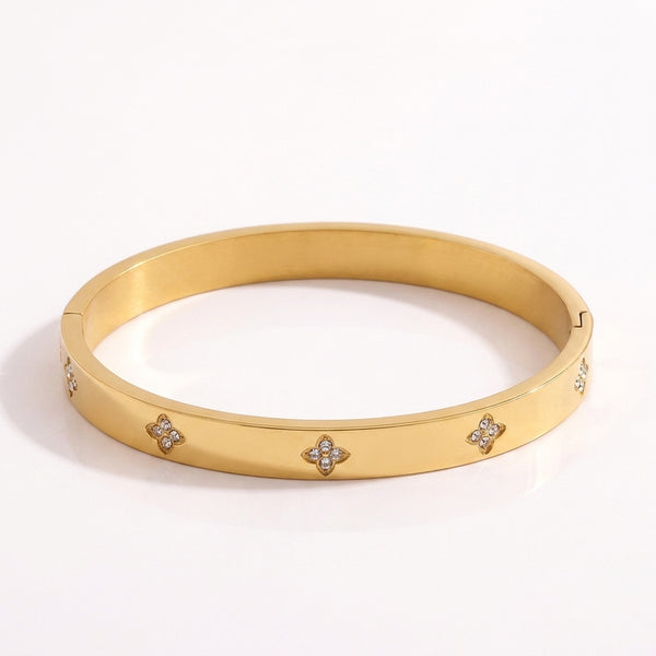 Close-up of a radiant gold-plated titanium steel bangle bracelet featuring sparkling diamond clover motifs on a pristine white background.