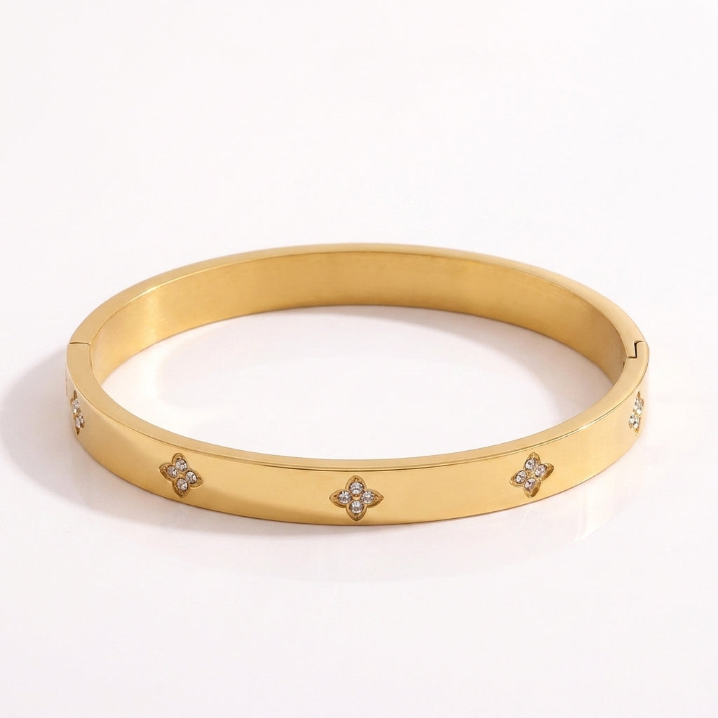 Close-up of a radiant gold-plated titanium steel bangle bracelet featuring sparkling diamond clover motifs on a pristine white background.