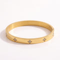 Close-up of a radiant gold-plated titanium steel bangle bracelet featuring sparkling diamond clover motifs on a pristine white background.
