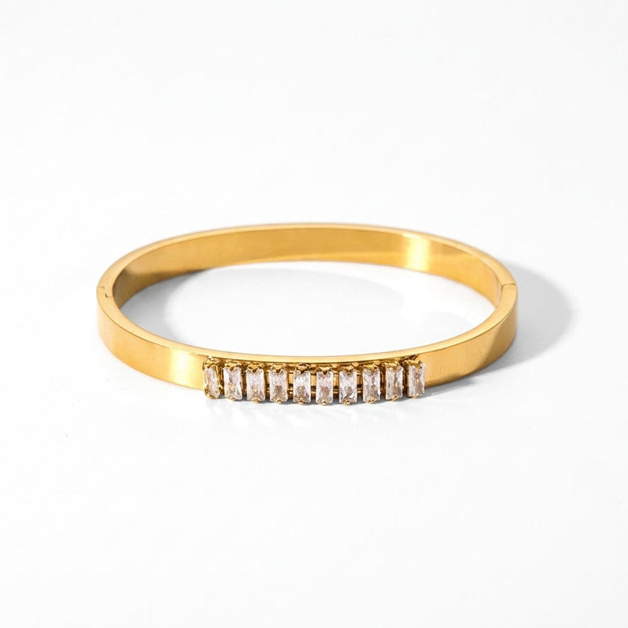 Elegant gold-plated stainless steel bangle bracelet with sparkling baguette zirconia stones on a white background.