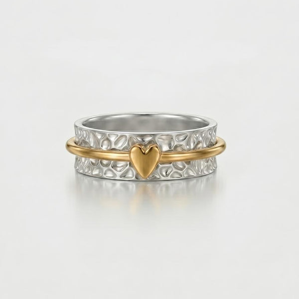 Silver ring with a gold heart charm on a light gray background